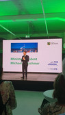 Ein Mann im Anzug steht auf der Bühne und spricht vor einer großen Leinwand, auf der ein Stadtbild und die Worte "Ministerpräsident Michael Kretschmer" zu sehen sind. Auf der Leinwand sind auch das Logo des Freistaates Sachsen und das Branding der Veranstaltung zu sehen.
