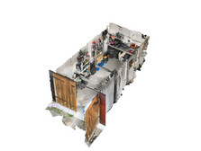 A 3D model of a small, cluttered workshop with various tools and materials on shelves on the walls. There is a workbench in the centre and a large, partially open wooden door at one end. The floors and walls show signs of heavy use.